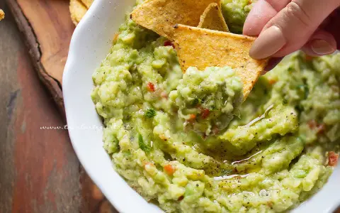 Un chip di mais raccoglie il cremoso guacamole, mostrando come fare il guacamole fresco e delizioso.