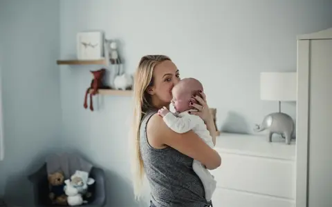 Mama tuli noworodka, który ma czkawkę. W tle pokój dziecięcy z pluszakami.
