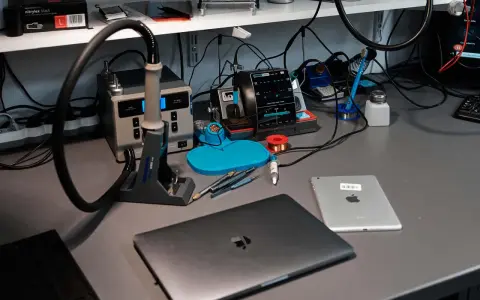 Na biurku serwisowym leży zamknięty laptop, obok tablet. W tle widać stację lutowniczą i narzędzia.