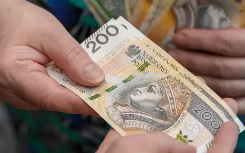 Dwie dłonie przekazują sobie banknot 200 zł. Czy opieka nad dzieckiem niepełnosprawnym wlicza się do emerytury?