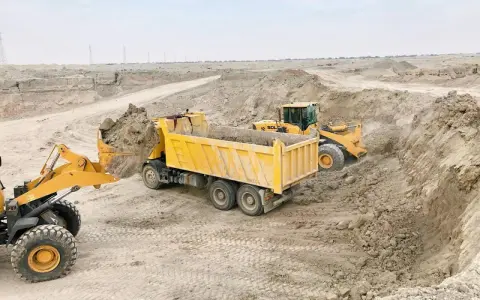 Ładowarka zasypuje ziemią wywrotkę na placu budowy. Spedycja wywrotki w akcji.