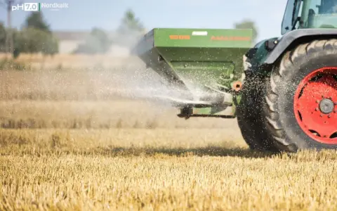 Traktor rozsiewa wapno magnezowe na polu.