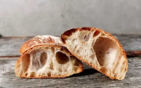 Zwei Hälften eines rustikalen ciabatta mit sauerteig, mit großer, luftiger Krume und knuspriger Kruste, liegen auf einem Holzbrett.