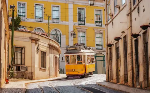 Gelbe Straßenbahn fährt durch enge Gassen Lissabons. Perfekt für angenehme Portugal Temperaturen im Mai.