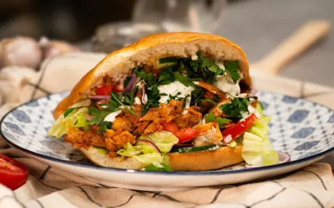 Pyszny, domowy kebab z kurczaka z piekarnika, pełen świeżych warzyw i sosu, na ozdobnym talerzu.