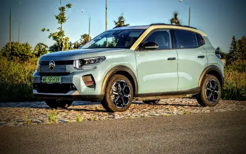 Jasnoszary Citroën ë-C3 z żółtym dachem stoi na tle drzew i nieba.
