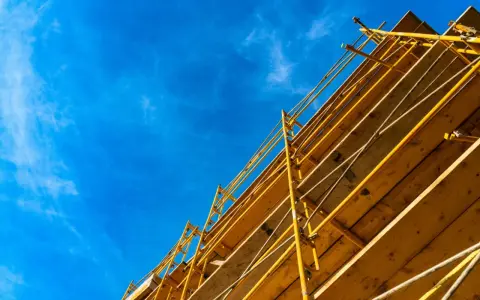 Estructura amarilla de madera y metal, que es una cimbra, contra un cielo azul con nubes finas.