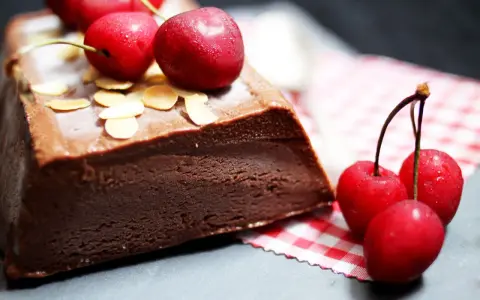 Une délicieuse marquise au chocolat, garnie de cerises fraîches et d'amandes effilées, prête à être dégustée.