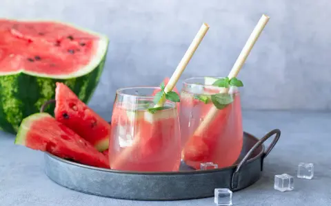 Orzeźwiający drink z arbuzem i miętą, podany na tacy z kawałkami arbuza i kostkami lodu. Idealny na upalne dni.