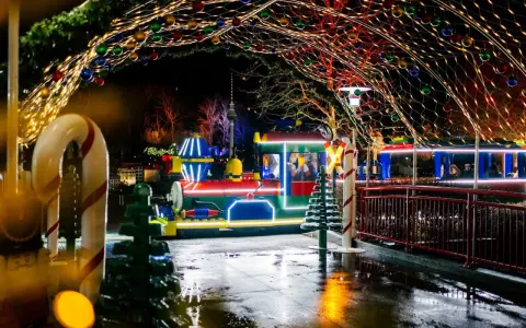 Ein bunter Zug fährt durch eine festlich beleuchtete Gasse im winterwonder legoland. Lichterketten und Kugeln schmücken den Weg.