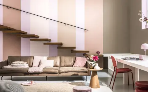 Un confortable canapé en cuir marron est installé sous un escalier flottant en bois. La pièce est décorée de coussins roses et d'un tapis en jute.