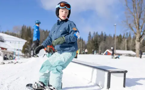 Barn åker snowboard i backen, redo att åka slalom. Solen skiner och snön ligger djup.