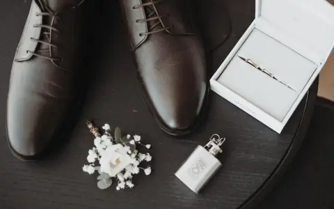 Eleganckie brązowe buty męskie, butonierka, pierścionki w pudełku i piersiówka.