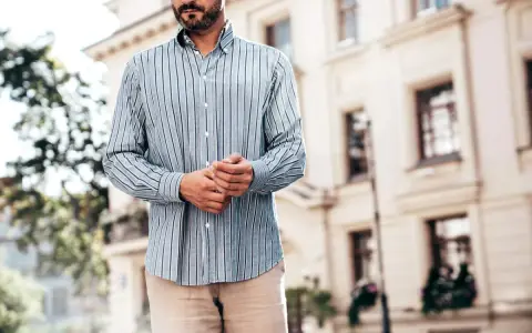 Mężczyzna w paski koszuli, z rękami złożonymi na brzuchu, idealnie pokazuje, kiedy koszula w spodnie tworzy elegancki look.