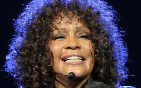Whitney Houston z zamkniętymi oczami, w pełni emocji, pokazuje niesamowitą **skalę głosu**.