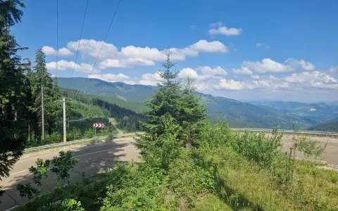 Górzysty krajobraz Rumunii z krętą drogą i lasami. W oddali widać pasma górskie, a na niebie chmury.