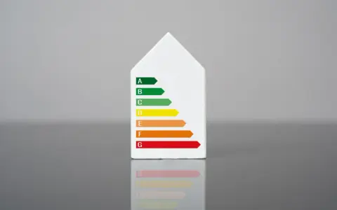 Biały model domu z naklejką klasy energetycznej. Świadectwo energetyczne mieszkania ocenia jego efektywność.