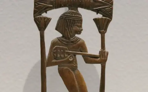 Sculpture en bois d'un musicien égyptien jouant d'un instrument ancien, ornée de motifs floraux.