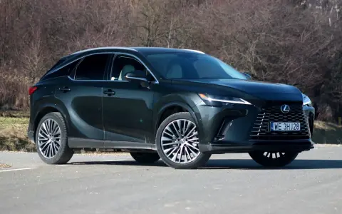 Ciemnozielony Lexus 450h z eleganckimi felgami stoi na drodze, otoczony suchymi krzewami.