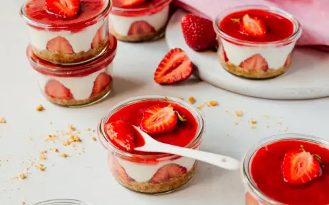 Mehrere kleine Gläser mit einem cremigen Dessert mit Erdbeeren und einer roten Erdbeersauce.