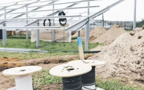 Na placu budowy paneli słonecznych przygotowywane są kable do uziemienia. Widać szpule z przewodami i metalowe konstrukcje.