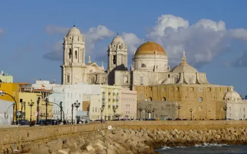 Die Kathedrale von Cadiz, ein majestätisches Bauwerk mit goldenen Kuppeln, ragt über bunte Häuser am Meer auf.
