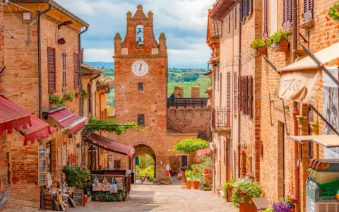 Un vicolo pittoresco a Gradara e dintorni, con case in mattoni, negozietti e un'antica torre dell'orologio.