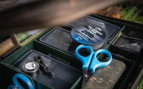 Alles für die beste Karpfenmontage: Fluorocarbon-Schnur, Schere und Zubehör in einer Tacklebox.