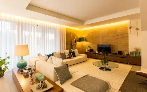 Salón moderno con sofá blanco, mesa de centro de cristal y **luz indirecta** que ilumina la pared de piedra y las cortinas.
