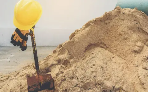 Żółty kask i rękawice na łopacie, obok sterty piachu. Zastanawiasz się, ile waży metr sześcienny piachu?
