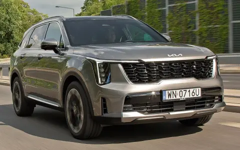 Nowa Kia Sorento w kolorze szarym, z charakterystycznym grillem i nowoczesnymi światłami, pędzi po drodze.