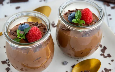 Zwei Gläser mit luftiger Schokomousse, garniert mit frischen Beeren und Schokostückchen. Ein Genuss für Schokoladenliebhaber!