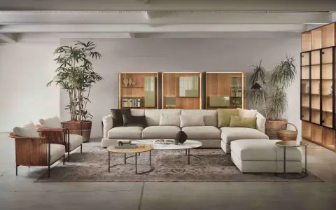 Un salotto moderno con divano componibile color tortora, poltrone in vimini e piante verdi.