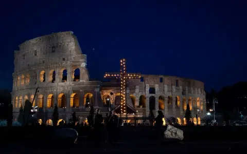 Colosseo illuminato di notte con una croce luminosa, un'atmosfera suggestiva che ricorda quando si festeggia Pasqua.