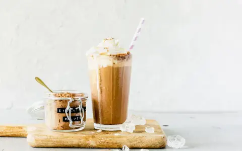 Eiskaffee mit gekochtem Kaffee, zubereitet im Thermomix, gekrönt mit Sahne. Daneben ein Glas mit Eiskaffee-Pulver.