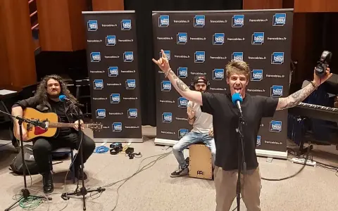 Un groupe rock alternatif français en pleine performance, avec un guitariste, un percussionniste et un chanteur énergique.