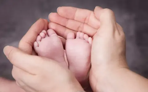 Manos adultas sostienen delicadamente los pies de un bebé. A partir de la semana 37, un bebé puede nacer.