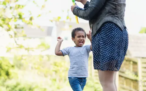 Ein 3-jähriges Kind hat einen Wutanfall, während eine Person Seifenblasen macht.