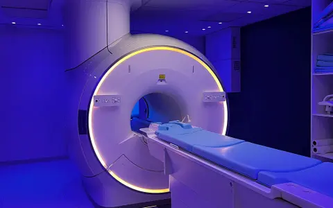 Nowoczesny aparat do rezonansu magnetycznego, z niebieskim łóżkiem pacjenta i podświetlanym tunelem. Tak wygląda rezonans magnetyczny.