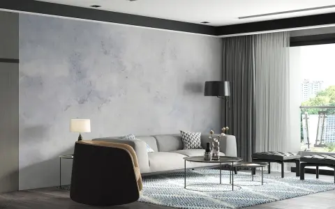 Nowoczesny salon z szarą sofą i fotelem. W tle efektowny **beton na ścianie**, który nadaje wnętrzu industrialnego charakteru.