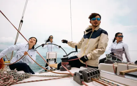 Kto to jest skipper? Młody mężczyzna w okularach przeciwsłonecznych kieruje jachtem, podczas gdy jego załoga pracuje przy linach.