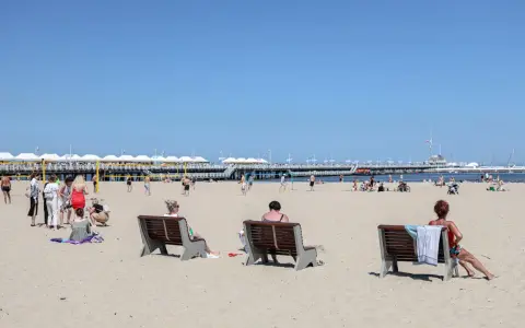 Ludzie odpoczywają na plaży, ciesząc się słońcem i widokiem na molo. To idealne miejsce na polską riwierę.