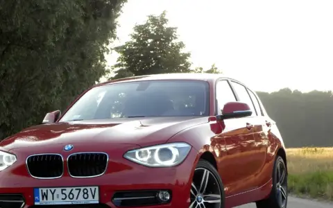 Czerwone BMW 118d na tle drzew i pól.