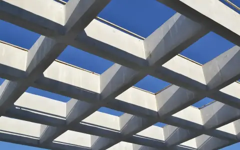 Estructura geométrica de vigas de hormigón armado, creando un patrón de cuadrados contra el cielo azul.