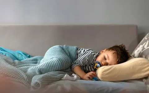 Mały chłopiec śpi na kanapie, otulony kocykiem. Wygląda na to, że mimo początkowego buntu, kiedy dziecko rezygnuje z drzemki, w końcu uległ zmęczeniu.