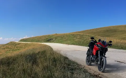 Ducati rossa ferma su strada sterrata, con un passo branchetto sullo sfondo e cielo azzurro.