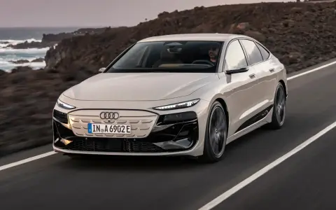 Jasnoszary Audi A6 e-tron jedzie po drodze z widokiem na ocean i góry.
