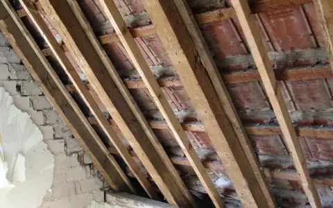 Charpente en bois avec des tuiles rouges et un mur en briques décrépit. Les contre latte sont visibles, soutenant la structure.