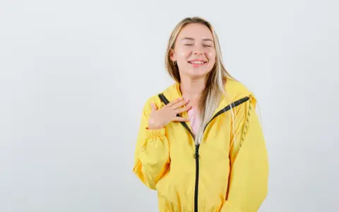 Uśmiechnięta blondynka w żółtej kurtce softshellowej, która przypomina jej, jak prać softshell, by zachować jego właściwości.