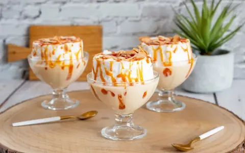 Trois coupes de crème anglaise avec une île flottante meringuée, nappées de caramel et d'amandes effilées.